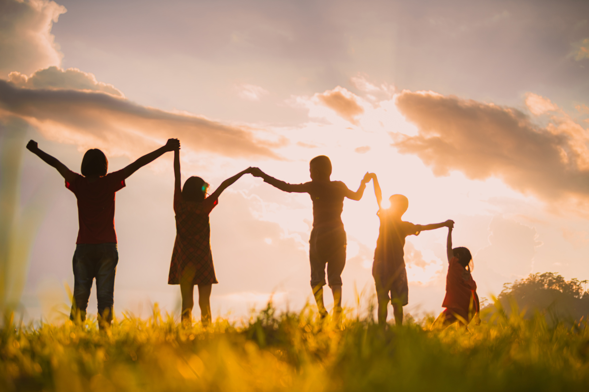 Mit einem Sonnenuntergang im Hintergrund halten sich fünf Kinder an den Händen.