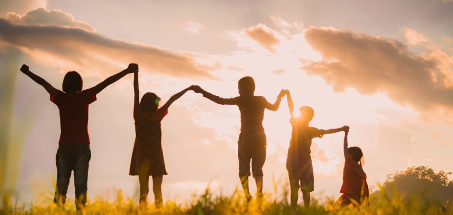 Mit einem Sonnenuntergang im Hintergrund halten sich fünf Kinder an den Händen.