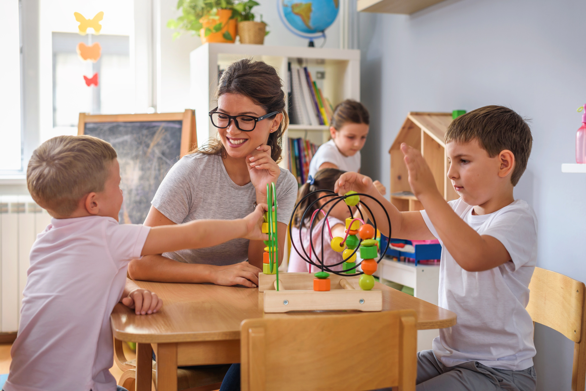 Eine junge Frau spielt mit drei Kindern und buntem Holzspielzeug.