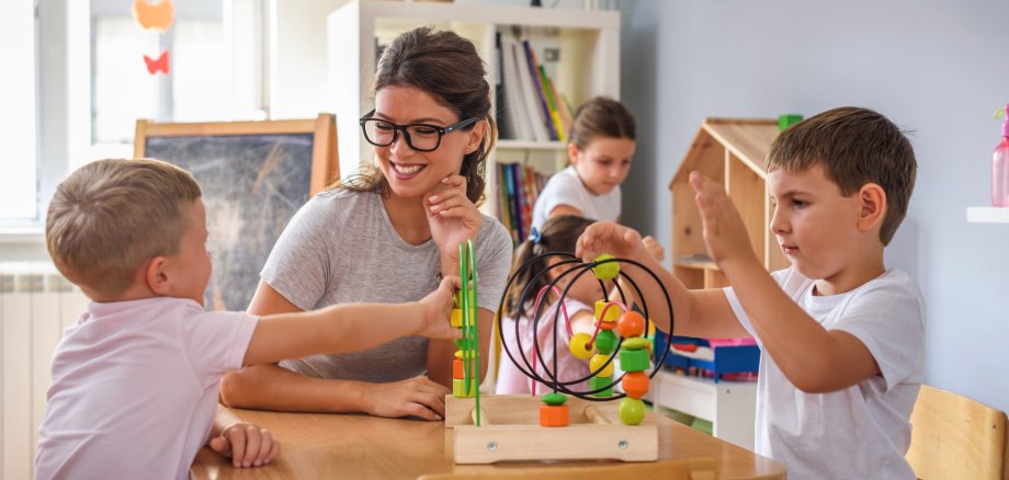 Eine junge Frau spielt mit drei Kindern und buntem Holzspielzeug.