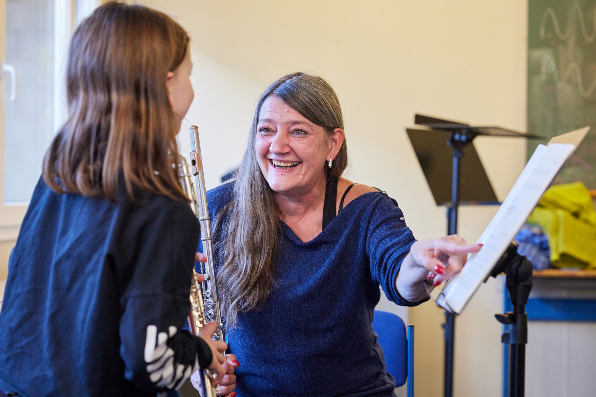 Eine Frau erklärt einem Mädchen mit Instrument Noten.