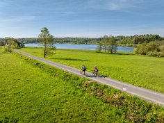 Zwei Radfahrer fahren entlang der Krombachtalsperre durch grüne Wiesen.