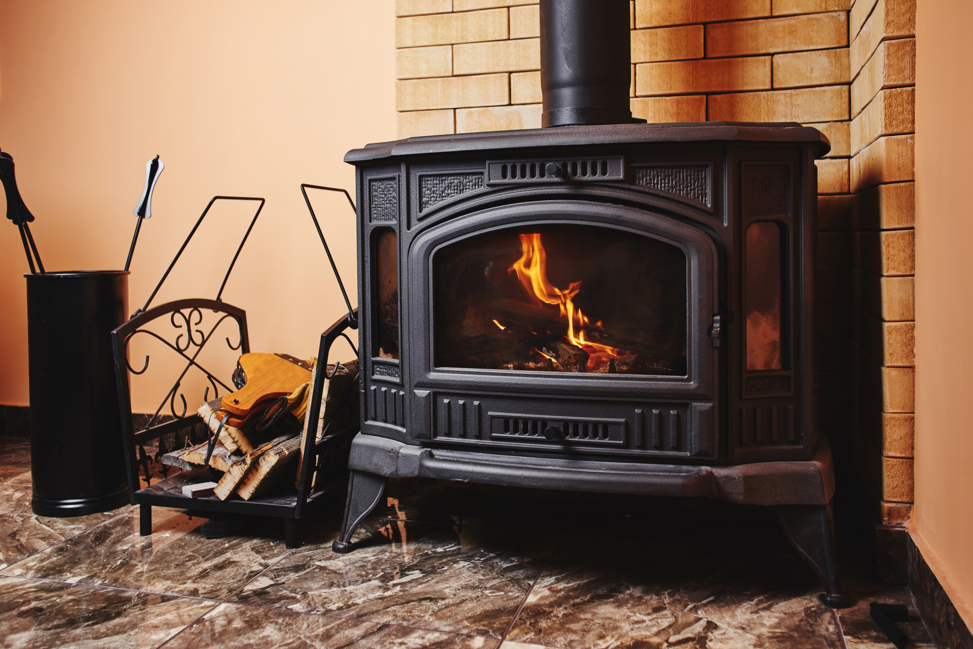 In einem Kamin brennt ein Feuer, daneben steht ein Korb mit Holz.