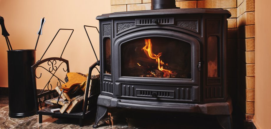 In einem Kamin brennt ein Feuer, daneben steht ein Korb mit Holz.