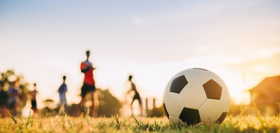 Die Silhouten von Kindern spielen auf Rasen Fußball.
