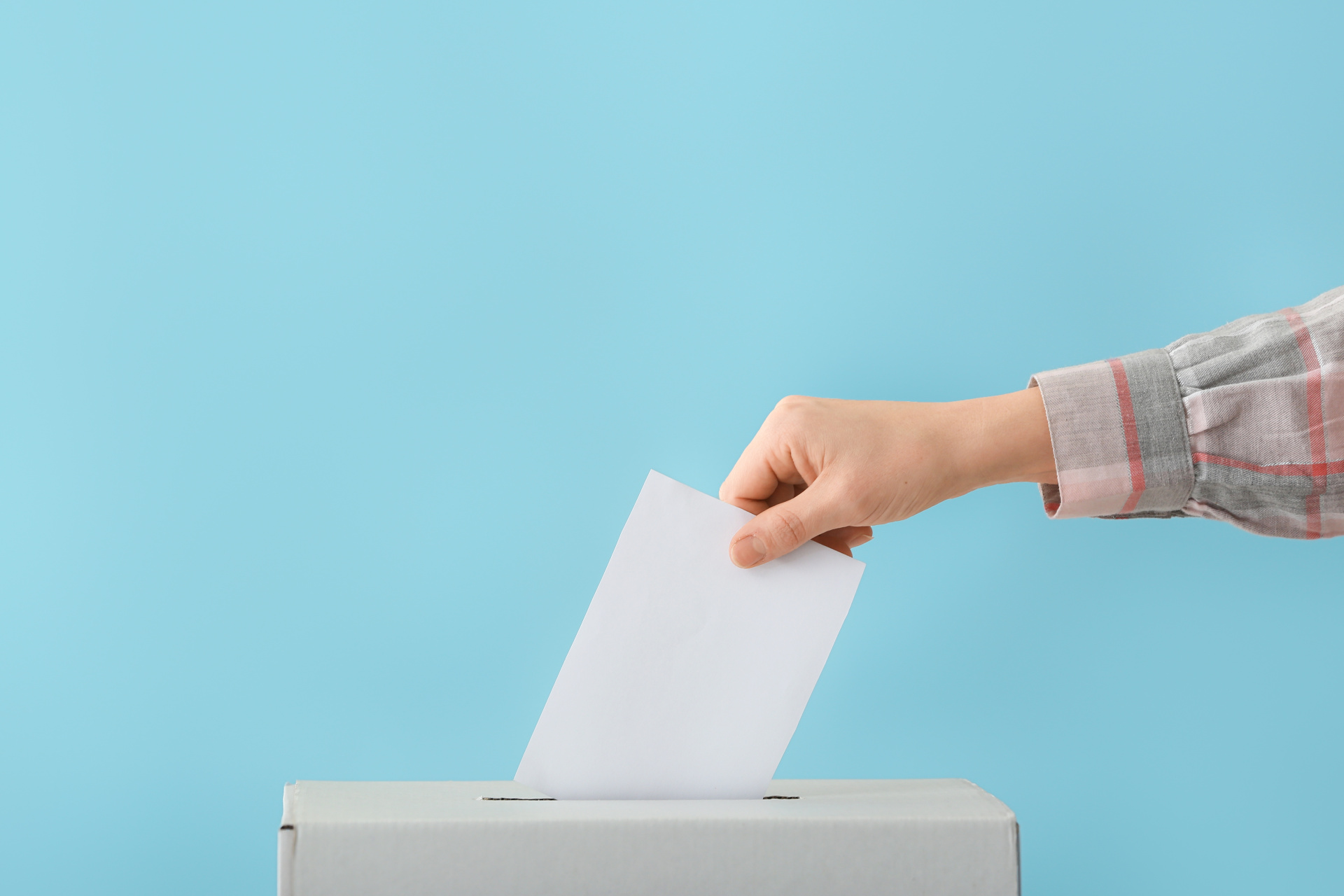 Eine Hand steckt einen Wahlzettel in eine Urne.