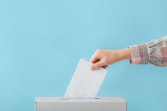 Eine Hand steckt einen Wahlzettel in eine Urne.