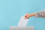 Eine Hand steckt einen Wahlzettel in eine Urne.