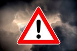Piktrogramm eines Warndreiecks mit Ausrufezeichen vor dramatischem Unterwetterhimmel als Symbol für Unwetterwarnung.