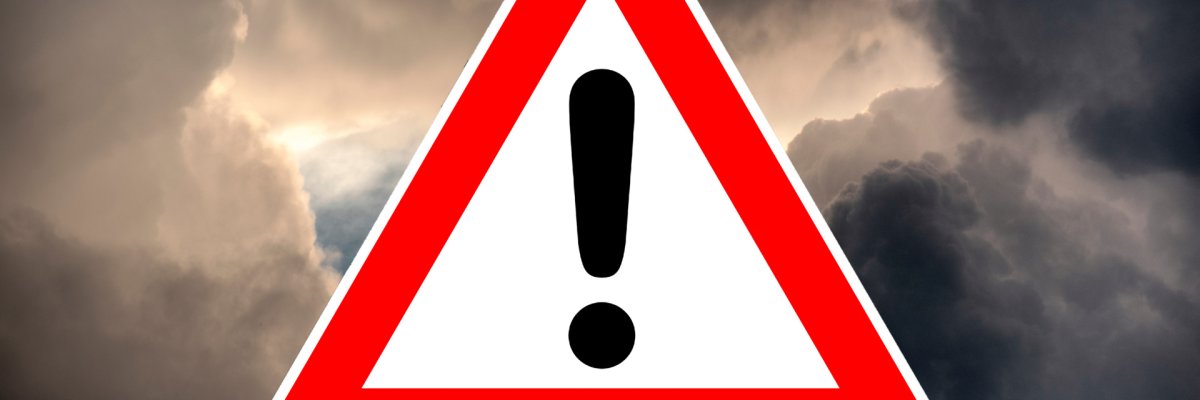 Piktrogramm eines Warndreiecks mit Ausrufezeichen vor dramatischem Unterwetterhimmel als Symbol für Unwetterwarnung.