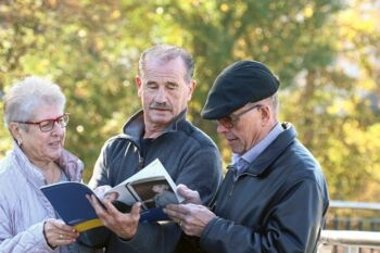 Zwei ältere Männer und eine Seniorin schauen in einen Flyer.